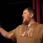 an actor on stage in front of red curtain performing a Shakespearean monologue