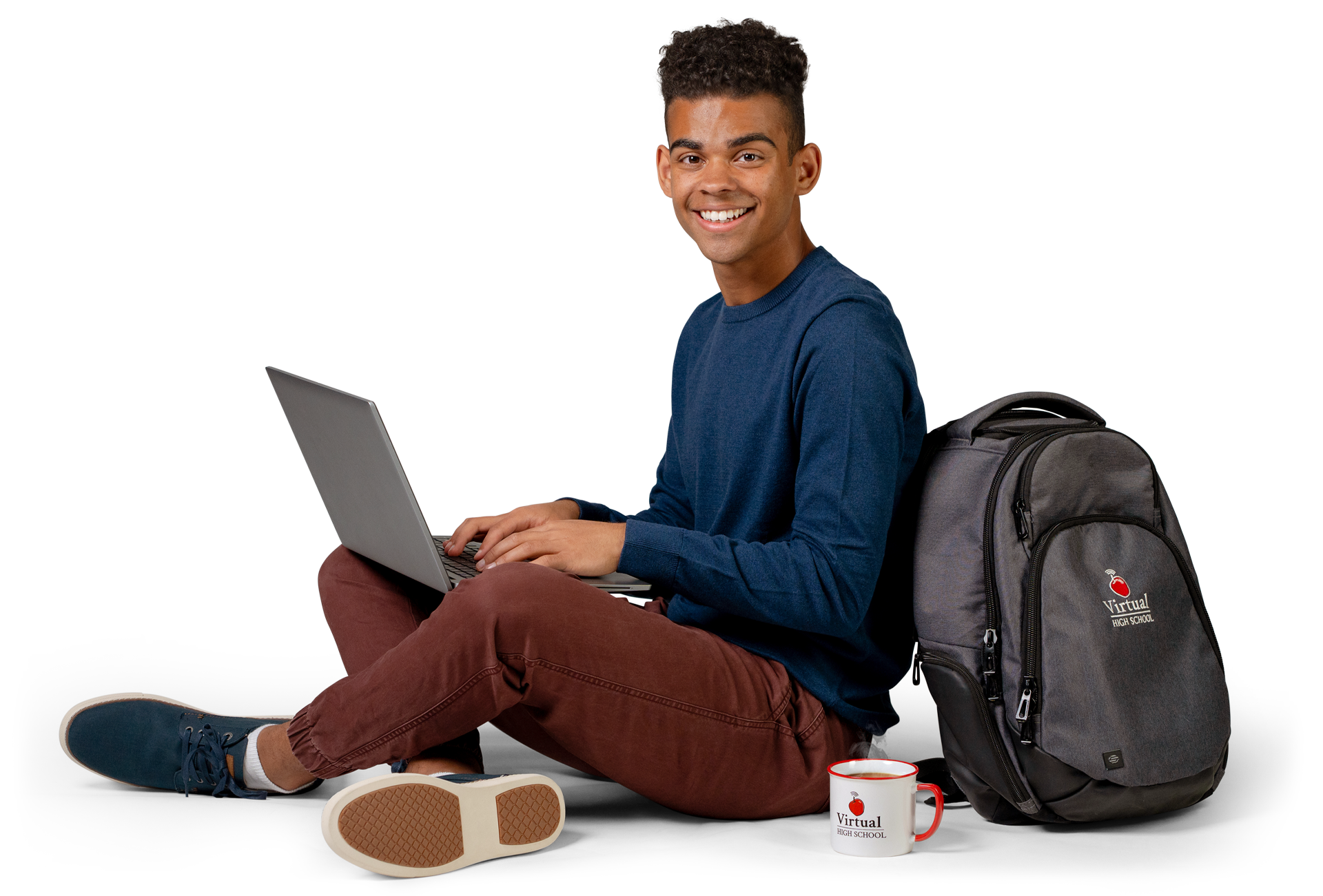 A young man sitting on the floor with a laptop, backpack, and a mug.