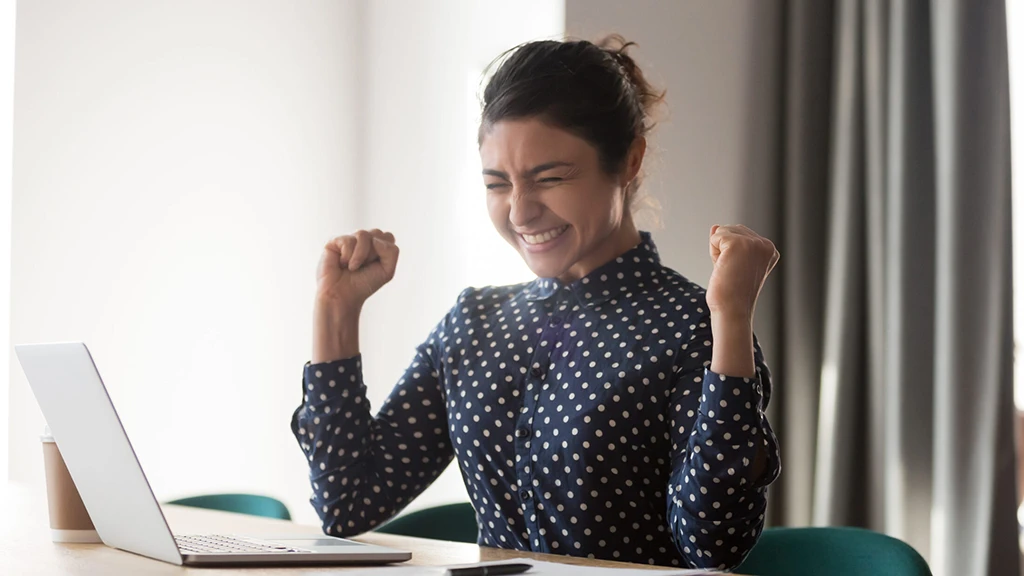 A student is celebrating in front of a laptop.