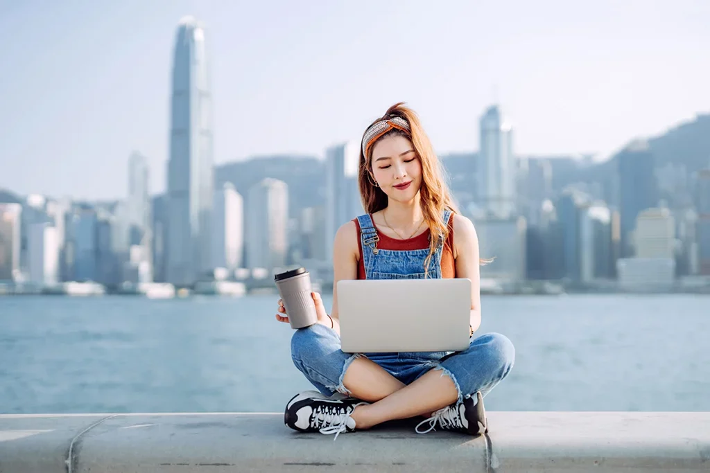 A student sitting on a ledge with a laptop and a cup of coffee.