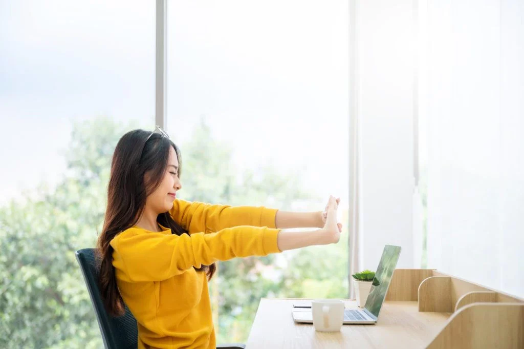 Asian woman stretching at her desk at home.