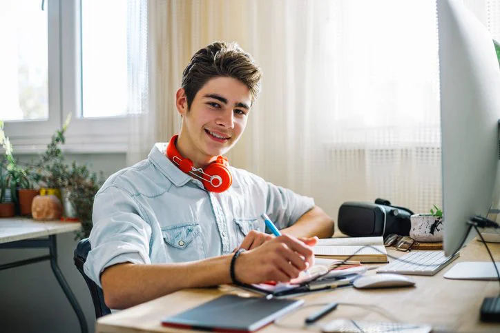 Portrait of a happy and satisfied student sitting at the table and a computer and do your homework, writing, reading, learning.