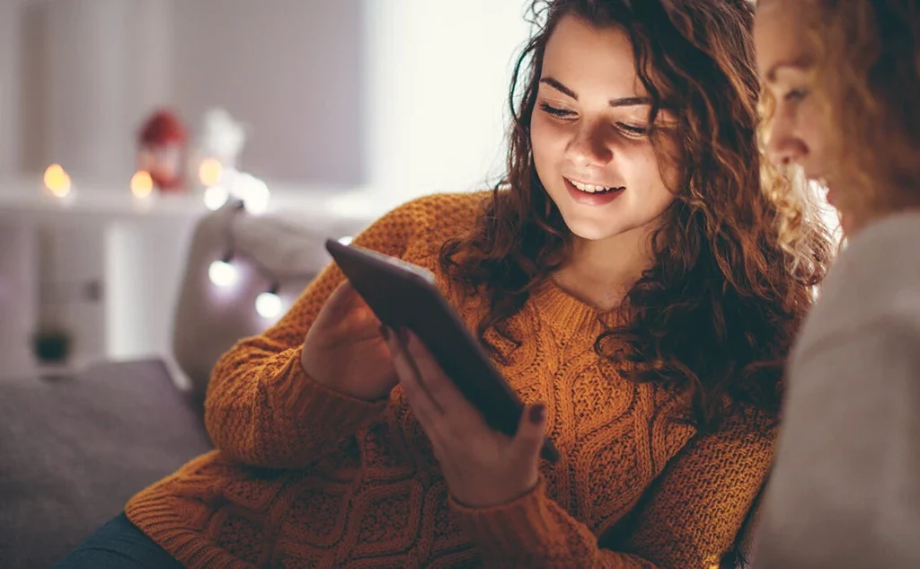 Two women sitting on a couch looking at a tablet.