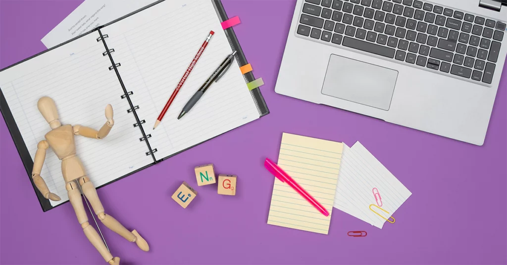 a notepad, laptop, drawing mannequin, pens and pencils, sticky notes, paperclips, and ENG letter blocks.